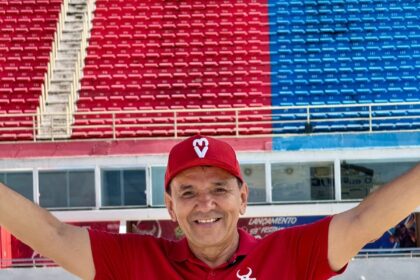 Homem de camisa vermelha e braços abertos posa em espaço cultural de Manaus durante anúncio de pré-candidatura política.